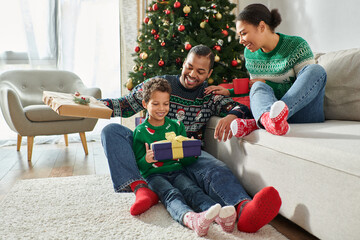 joyous african american woman looking lovingly at her husband and son exchanging presents, Christmas