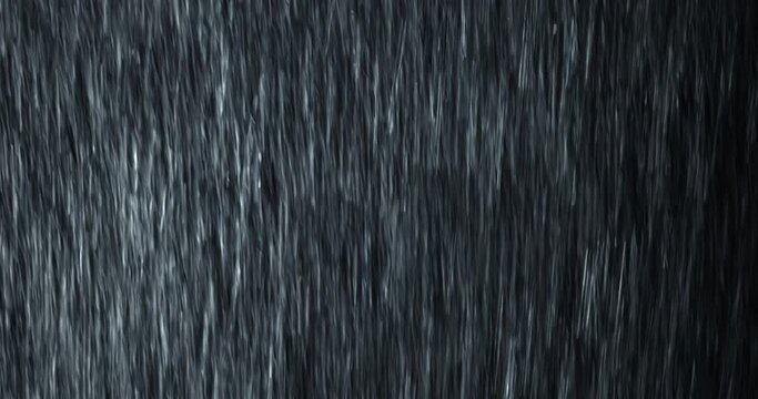 A heavy rain wall falls in front of the black screen in 4K loopable high-speed footage. Raindrops splashing. Rain closeup VFX insert. Practical, seamlessly loopable. Heavy rainstorm hitting black.