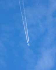 An airplane crossing the blue sky leaving a white trail of steam.