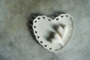 Overhead view of a white heart shaped dish with two heart shaped ornaments on a grey background