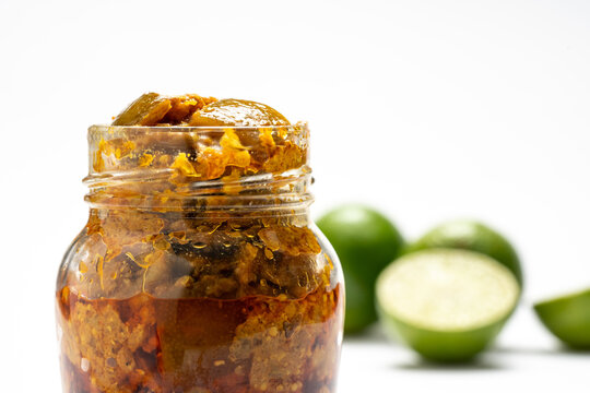 Homemade Indian spicy lime pickle with salt, chilli, pepper in a glass jar againt a white background.