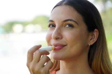 Close-up of smiling young woman applying sun protection on her lip outdoor - obrazy, fototapety, plakaty