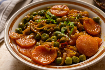 Homemade spicy carrots with green peas curry cooked north Indian style with onions and spices served in a white bowl.  Close-up, selective focus.