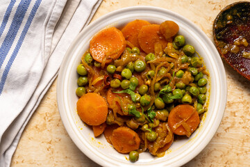 Homemade spicy carrots with green peas curry cooked north Indian style with onions and spices served in a white bowl. Top view.