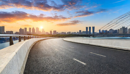 asphalt road and bridge with city skyline at sunset