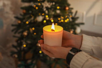 Burning candle in hands on a Christmas tree background
