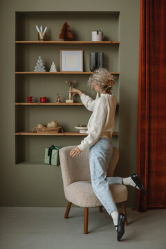 Rear view of a woman arranging festive Christmas ornaments on a bookshelf in her living room