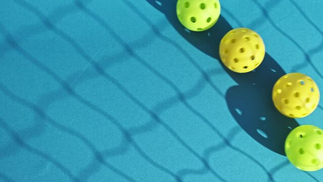 overhead image of yellow and green pickleball balls rolling down a blue court with the shadow of a net cast on the ground
