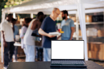Image showcasing laptop displaying isolated white screen placed on table while group of volunteers...