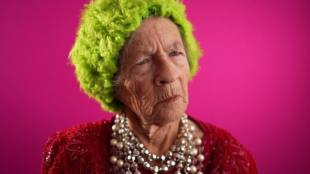 Unhappy displeased fisheye view caricature of funny elderly woman with green wig or hat isolated on pink background in slow motion.