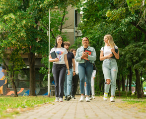 Shot of a couple high school or university students talking and walking together outside the school with backpacks and books in their hands