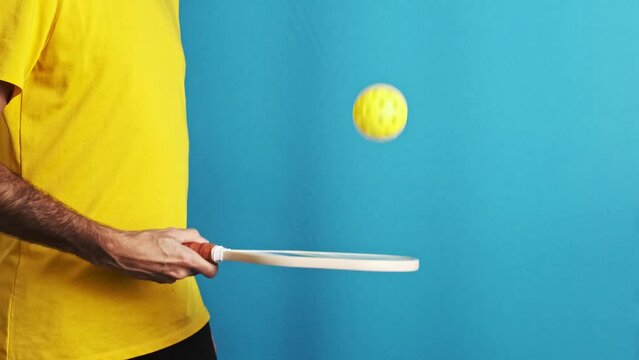 unrecognizable man in yellow t-shirt tapping controlling a pickleball ball in slow motion on blue background