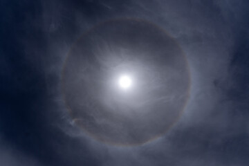 Naklejka na ściany i meble A 22° halo is an atmospheric optical phenomenon that consists of a halo with an apparent radius around the Sun or Moon. Also known as a moon ring, storm ring, or winter halo Sun rainbow