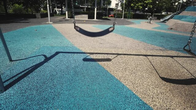 Empty children's playground at the park with a swing swinging in a sunny weather