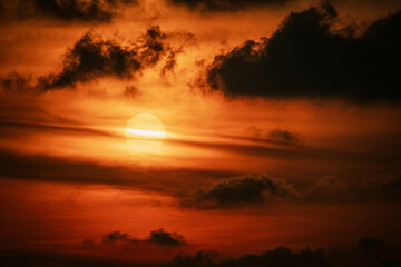 Scenic red orange Sunset with Sun hiding in clouds, glowing light line crosses Sun disk horizontally, close up photo. Thailand