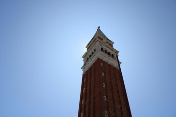 Tall tower of St Mark's Campanile with a clock at the top of it against the blue sky