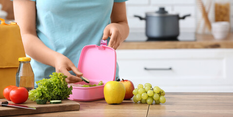 Woman packing fresh food into lunch box in kitchen