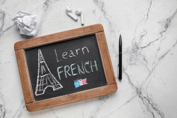 Chalkboard with text LEARN FRENCH, earphones, pen and crumpled paper on grunge background