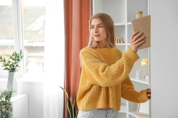 Young woman taking book from shelf at home