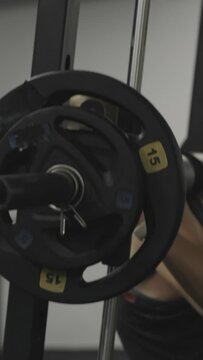 Vertical video. Woman in the gym doing squats in the Smith machine. Side view.