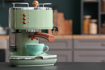 Modern coffee machine with cup on black table in kitchen, closeup
