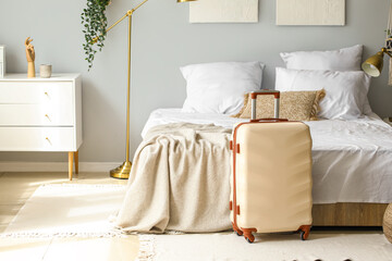 Big suitcase near bed in light room - obrazy, fototapety, plakaty