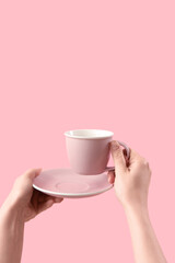 Female hands holding cup and saucer on pink background