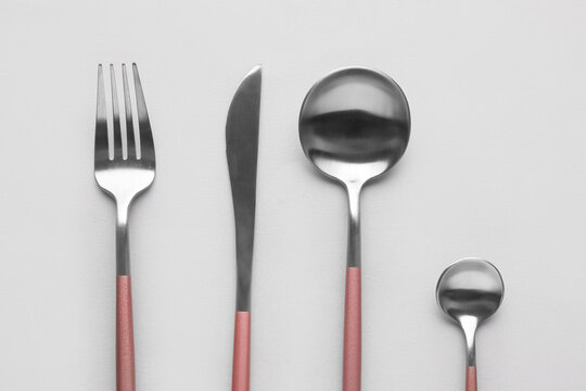 Silver fork, knife and spoons with pink handle on grey background