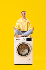 Pretty young woman meditating on washing machine against yellow background