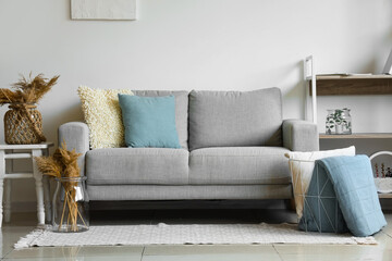Cozy grey sofa and basket with soft blanket in interior of living room - obrazy, fototapety, plakaty