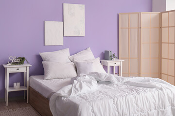 Interior of stylish bedroom with comfortable bed, white pillows, bedside tables and folding screen