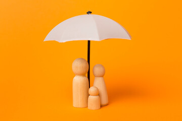 Wooden family figures under umbrella on color background.Insurance coverage concept. - obrazy, fototapety, plakaty