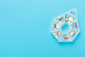 Daily pill organizer with medications on color background, top view