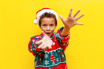 african american boy in christmas sweater and santa hat gives and throws on yellow isolated...