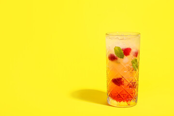 Glass of fresh raspberry mojito on yellow background