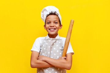 african american boy in chef's uniform and hat holding kitchen items and smiling on yellow isolated...