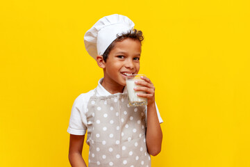 african american boy in chef's uniform and hat holding glass of milk on yellow isolated background