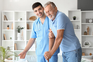 Obraz premium Male nurse helping senior man with stick to walk at home