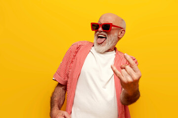 old grandfather pensioner in sunglasses shows rock gesture and sings to the music at party on...