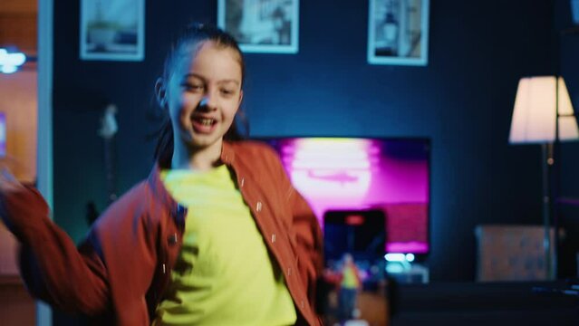 Children media star dancing in apartment, recording video with phone for gen z internet users. Happy girl filming herself with smartphone doing dance moves, following online choreographic trends