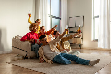 multiracial group of young friends sitting on the couch at home drinking beer and watching TV and celebrating good luck - obrazy, fototapety, plakaty