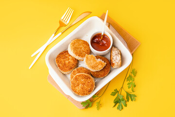 Baking dish of tasty meat cutlets on yellow background