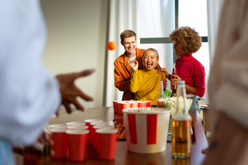 multiracial group of young friends playing beer pong at a party drinking beer and having fun at home
