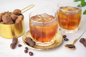 Glasses of tasty tamarind drink and fruits on white background