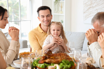 Happy family praying before dinner at festive table on Thanksgiving Day