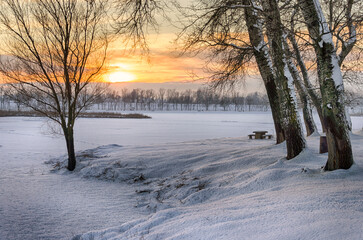 Snowy winter landscape with sunset in the background. The frozen Tisza backwater can be seen in Tiszalök, Hungary. Bare trees and branches are still visible in the picture. Hungarian rural landscape. 