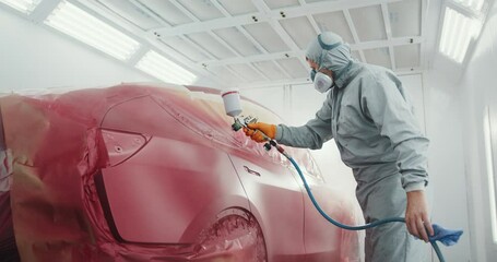 Automobile Repair. Person Spray Painting Car in Red Color in Special Car Chamber. Car Service Station. Worker Painting a Red Electric Car in Special Garage, Wearing Costume and Protective Gear