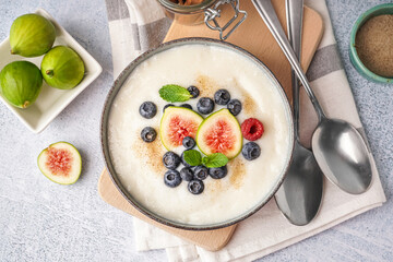 Bowl of tasty semolina porridge with fresh berries and figs on white background