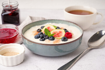 Bowl of tasty semolina porridge with fresh berries and figs on white background