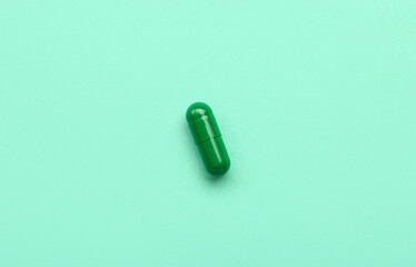 Green medical capsule on turquoise background